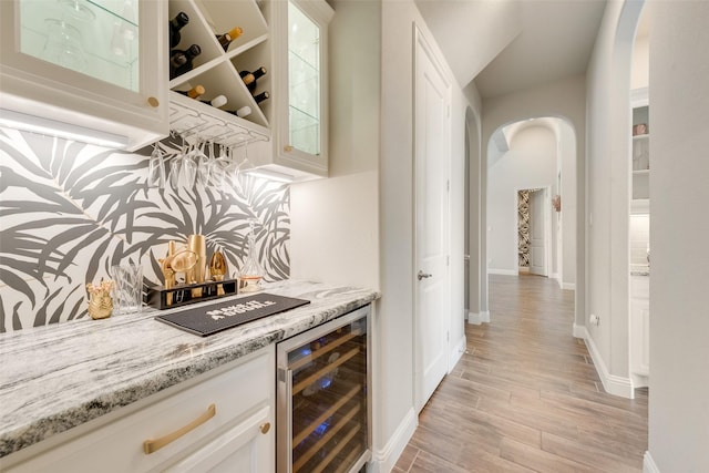 bar featuring light stone countertops, white cabinets, beverage cooler, and light wood-type flooring