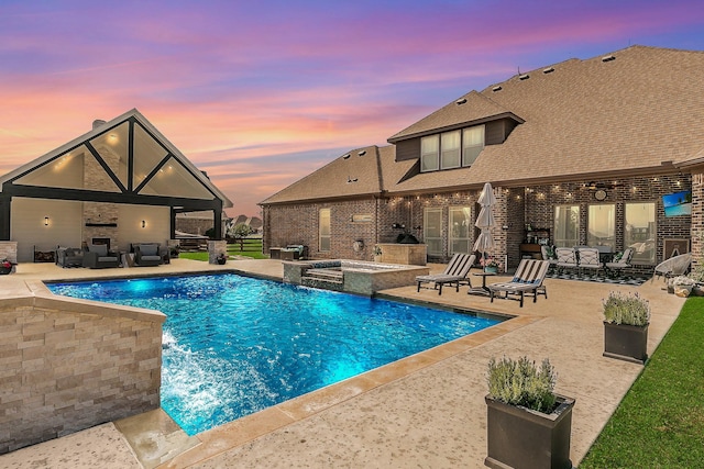 pool at dusk with an in ground hot tub, pool water feature, a patio area, and an outdoor fireplace