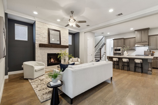 living room with hardwood / wood-style flooring, crown molding, a stone fireplace, and ceiling fan