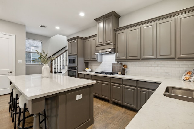 kitchen with sink, light stone counters, appliances with stainless steel finishes, dark hardwood / wood-style flooring, and decorative backsplash