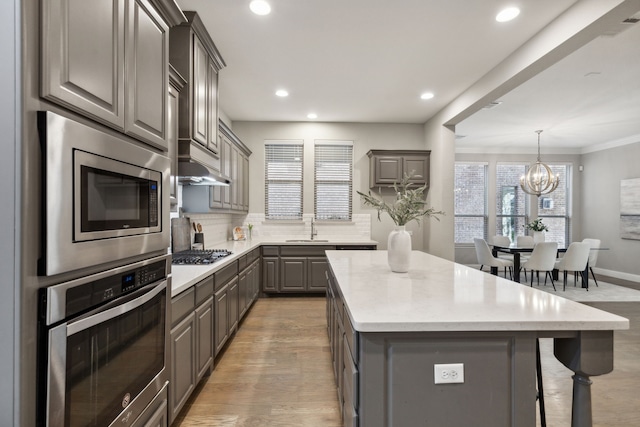 kitchen featuring sink, gray cabinets, hanging light fixtures, stainless steel appliances, and a center island