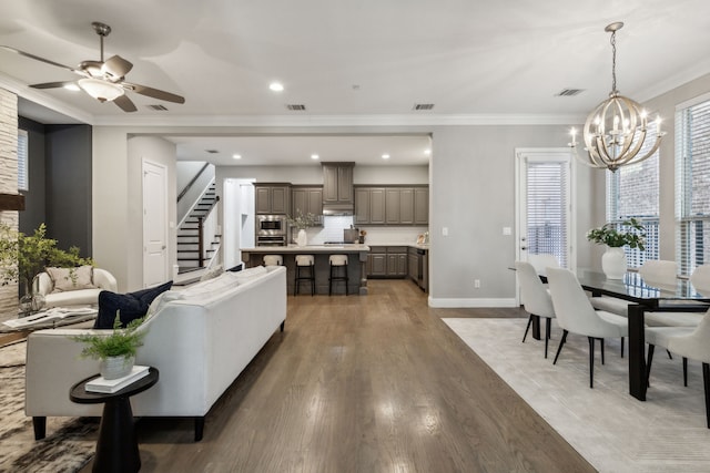 living room with ornamental molding, ceiling fan with notable chandelier, and wood-type flooring