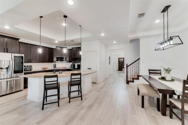 kitchen featuring appliances with stainless steel finishes, a tray ceiling, hanging light fixtures, and light hardwood / wood-style floors