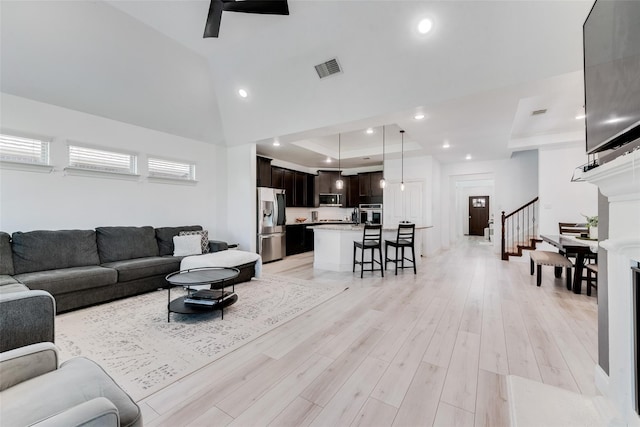 living room featuring light hardwood / wood-style floors, a raised ceiling, and ceiling fan