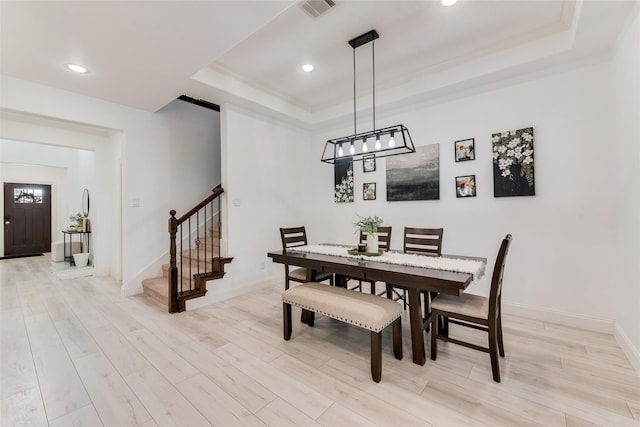 dining area with light wood-type flooring and a tray ceiling