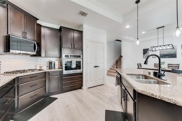 kitchen featuring sink, stainless steel appliances, backsplash, light hardwood / wood-style floors, and pendant lighting