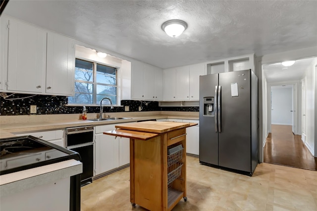 kitchen with stainless steel refrigerator with ice dispenser, sink, white cabinetry, tasteful backsplash, and a center island