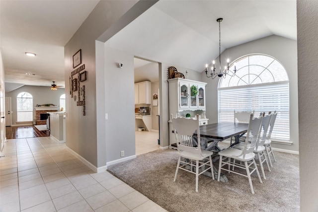 dining room featuring a brick fireplace, light tile patterned floors, vaulted ceiling, and ceiling fan with notable chandelier