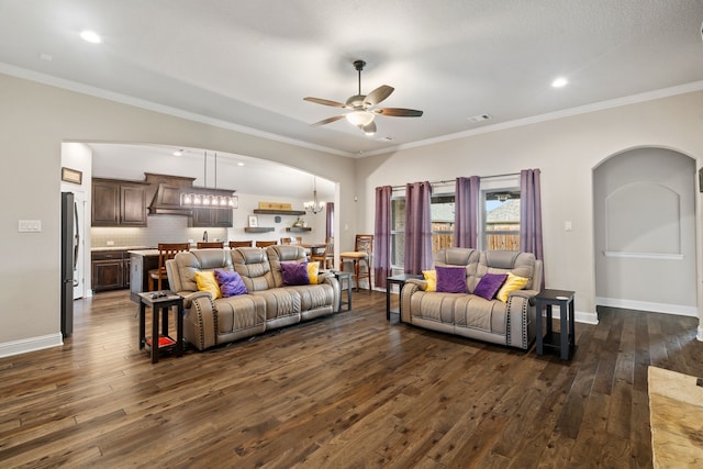 living room featuring crown molding, dark wood-type flooring, and ceiling fan with notable chandelier