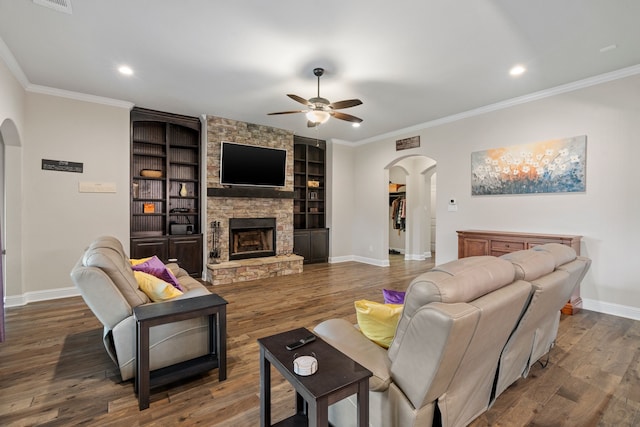 living room featuring crown molding, ceiling fan, wood-type flooring, built in shelves, and a stone fireplace