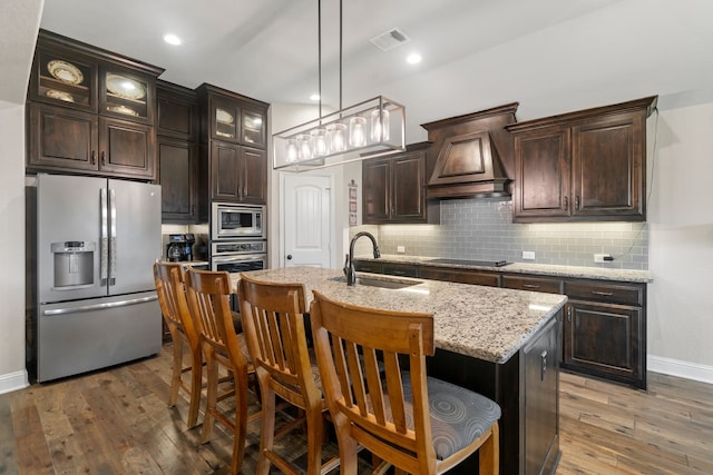 kitchen featuring premium range hood, a kitchen bar, sink, an island with sink, and stainless steel appliances