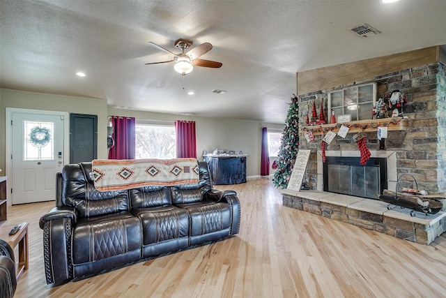 living room with hardwood / wood-style flooring, a fireplace, ceiling fan, and a textured ceiling