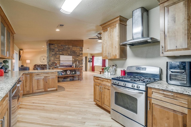 kitchen with gas range, light stone countertops, wall chimney range hood, and light hardwood / wood-style floors