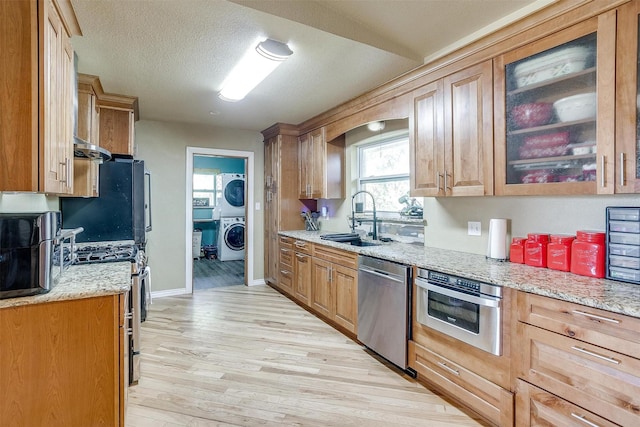 kitchen with light stone countertops, light wood-type flooring, a textured ceiling, stainless steel appliances, and sink