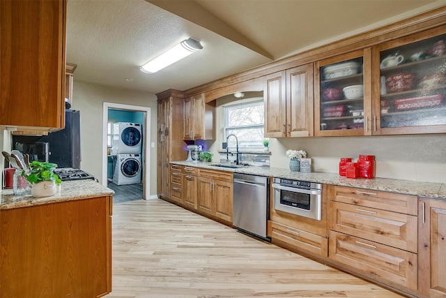 kitchen featuring light hardwood / wood-style flooring, stacked washer / dryer, stainless steel appliances, light stone countertops, and sink