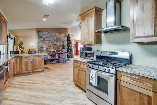 kitchen with stainless steel range with gas stovetop, light hardwood / wood-style flooring, plenty of natural light, and wall chimney range hood