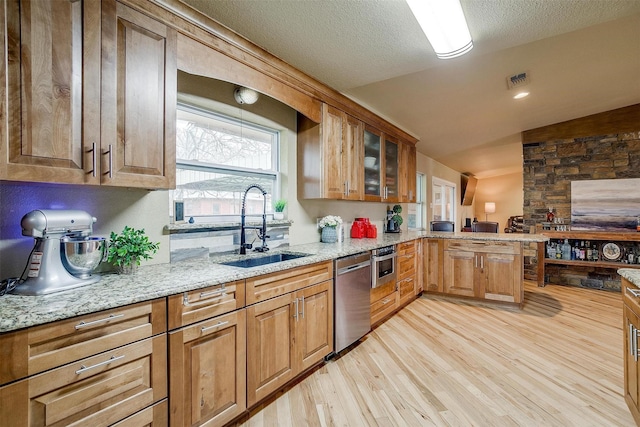 kitchen with appliances with stainless steel finishes, light hardwood / wood-style flooring, sink, and light stone countertops