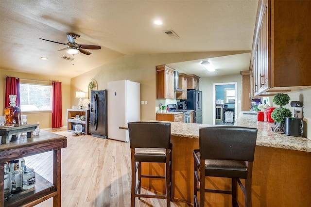 kitchen featuring light hardwood / wood-style flooring, black refrigerator, a breakfast bar, stainless steel range with gas cooktop, and kitchen peninsula