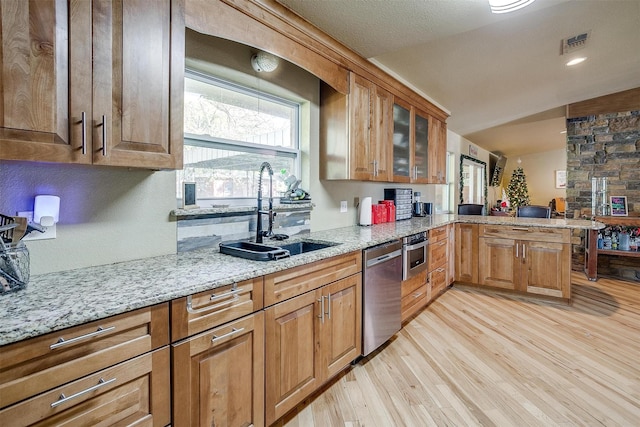 kitchen featuring sink, light hardwood / wood-style flooring, vaulted ceiling, light stone counters, and stainless steel appliances