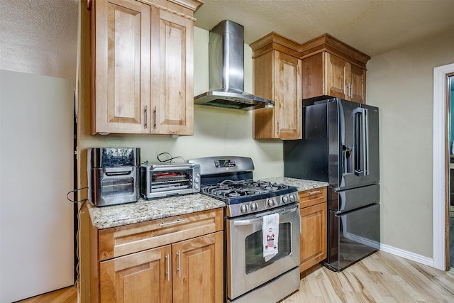 kitchen featuring light stone countertops, black refrigerator with ice dispenser, wall chimney exhaust hood, gas stove, and light hardwood / wood-style floors