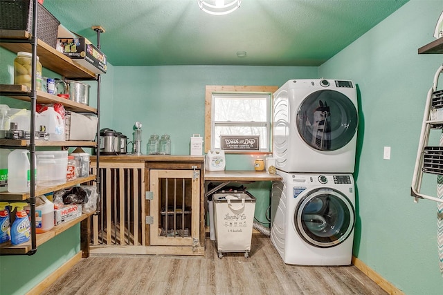 laundry room with a textured ceiling, light hardwood / wood-style floors, and stacked washer and clothes dryer