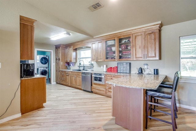 kitchen with plenty of natural light, kitchen peninsula, appliances with stainless steel finishes, and stacked washer and clothes dryer