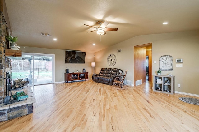 living area with ceiling fan, light hardwood / wood-style flooring, a stone fireplace, and lofted ceiling