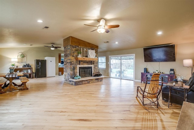 living room with light wood-type flooring, ceiling fan, lofted ceiling, and a stone fireplace