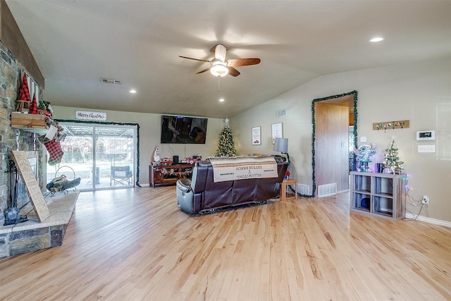 living room with ceiling fan, a stone fireplace, light wood-type flooring, and vaulted ceiling