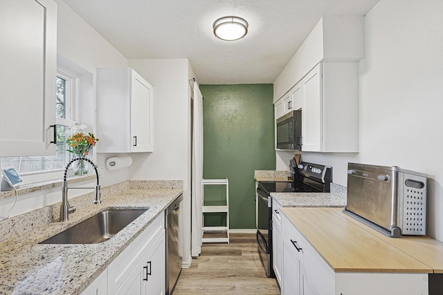 kitchen with black electric range oven, sink, stainless steel dishwasher, light stone counters, and white cabinetry