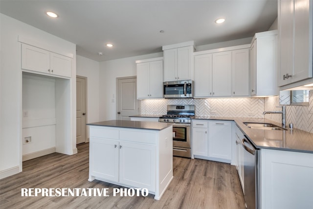 kitchen with light wood-type flooring, stainless steel appliances, sink, white cabinets, and a kitchen island