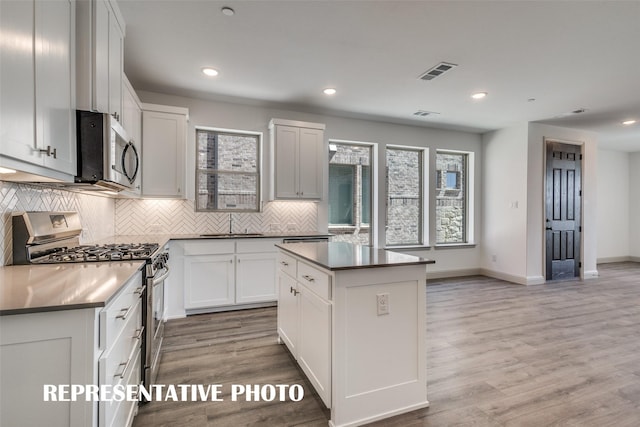 kitchen with appliances with stainless steel finishes, tasteful backsplash, white cabinets, a center island, and light hardwood / wood-style floors