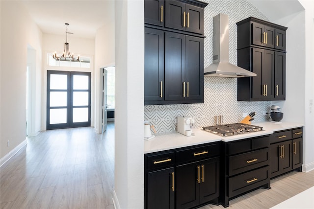 kitchen featuring light wood-type flooring, backsplash, wall chimney exhaust hood, pendant lighting, and stainless steel gas stovetop