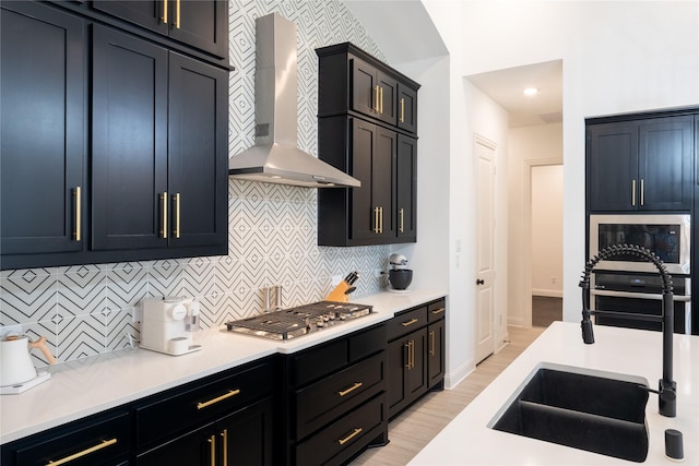 kitchen with stainless steel gas stovetop, backsplash, sink, wall chimney exhaust hood, and light wood-type flooring