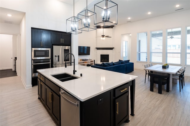 kitchen with a kitchen island with sink, sink, appliances with stainless steel finishes, decorative light fixtures, and a large fireplace