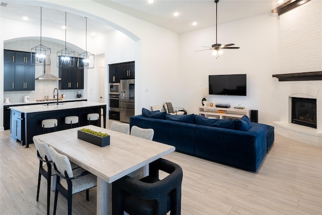 dining area featuring ceiling fan, a large fireplace, sink, and light hardwood / wood-style flooring