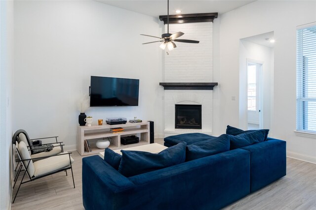 living room with a brick fireplace, ceiling fan, a healthy amount of sunlight, and light hardwood / wood-style floors