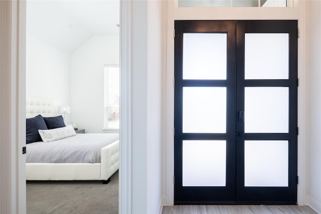 bedroom featuring french doors, light hardwood / wood-style floors, and lofted ceiling