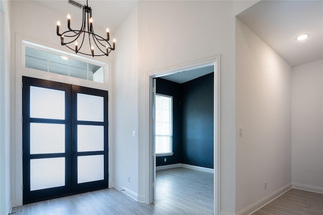 entryway with light hardwood / wood-style flooring, french doors, and an inviting chandelier