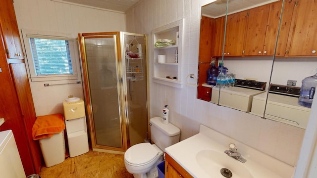 bathroom with toilet, wood walls, vanity, a shower with door, and washer and clothes dryer