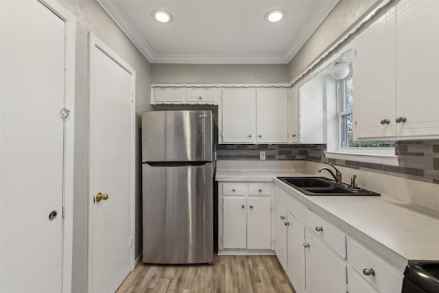 kitchen with stainless steel refrigerator, sink, white cabinets, decorative backsplash, and crown molding