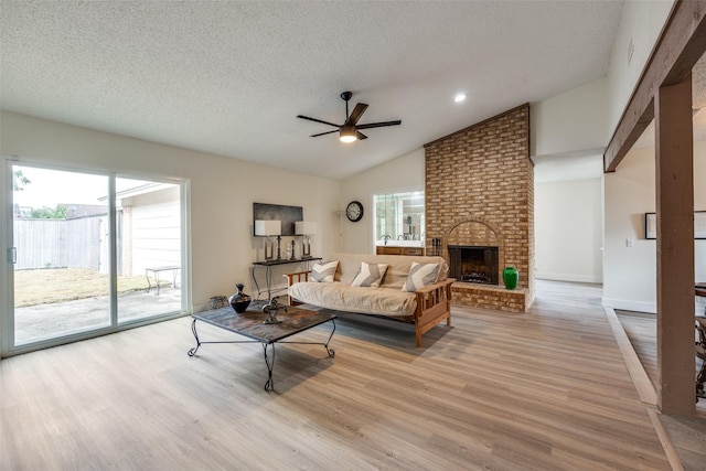 living room with a brick fireplace, ceiling fan, a textured ceiling, and light wood-type flooring