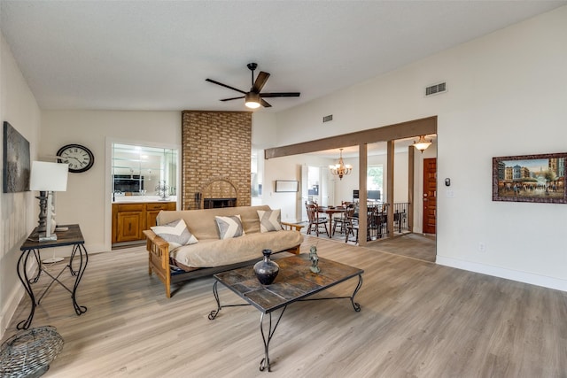 living room with a brick fireplace, ceiling fan with notable chandelier, light hardwood / wood-style flooring, and vaulted ceiling