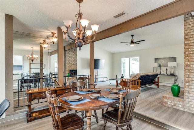 dining area featuring light wood-type flooring, a brick fireplace, ceiling fan with notable chandelier, a textured ceiling, and lofted ceiling with beams