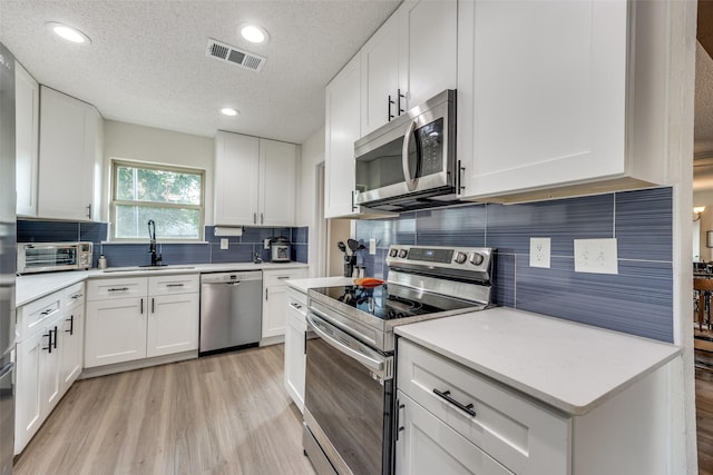 kitchen with appliances with stainless steel finishes, a textured ceiling, and white cabinetry