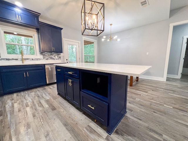 kitchen featuring blue cabinetry, sink, stainless steel dishwasher, light hardwood / wood-style floors, and decorative light fixtures