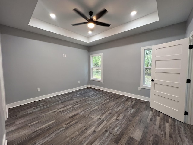 empty room with ceiling fan, dark wood-type flooring, a wealth of natural light, and a tray ceiling