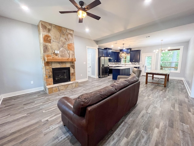 living room featuring a stone fireplace, ceiling fan with notable chandelier, and hardwood / wood-style flooring