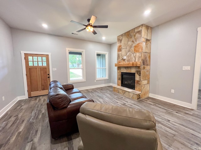 living room featuring wood-type flooring, a stone fireplace, and ceiling fan