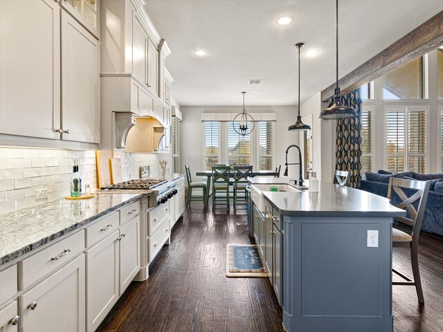 kitchen featuring hanging light fixtures, dark wood-type flooring, an island with sink, and a healthy amount of sunlight